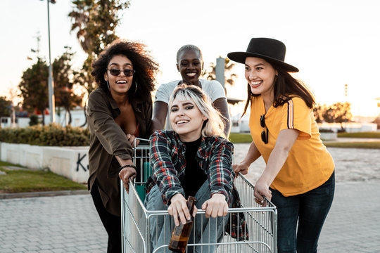 Multiracial Group Of Young Women Standing Around Shopping Cart On Road