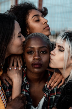 Portrait of young black short haired woman looking at camera with serious face while female friends supporting with hugs and kisses