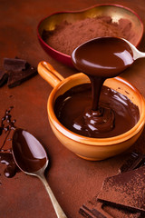 brown background, smeared with cocoa and chocolate chips, some pieces of chocolate and a bowl with melted dark chocolate