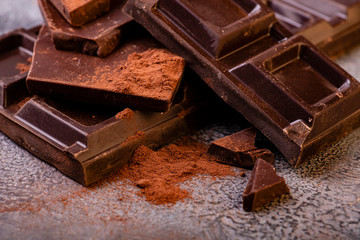 in the foreground stacked pieces of dark chocolate sprinkled with cocoa powder.