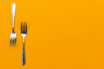 Two steel forks on an orange background. Cutlery for eating in a restaurant or at home. Stainless...