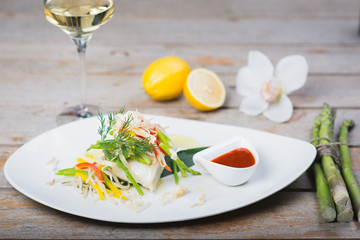 White fish seabass fillet with vegetables and white wine on a wooden table in a restaurant with decor. Tasty and healthy food. A cozy evening in a restaurant during a date. Beautiful table setting.