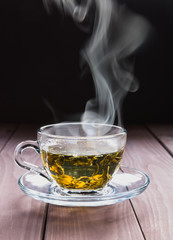 A transparent cup of hot green tea and steam on a dark background.