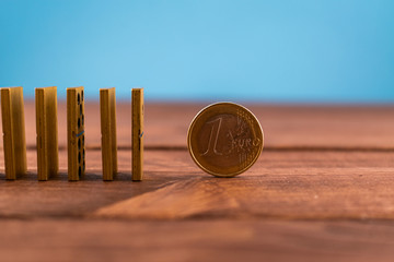 One euro coin and standing domino on a wooden backround. Finance, anticrisis concept.