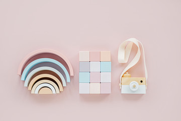 Wooden rainbow, colorful blocks and toy camera. Stylish baby toys on pastel pink background. Eco friendly, plastic free toys accessories for kids. Flat lay, top view