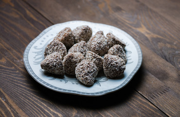 Chocolate candies in coconut shavings on a saucer on a wooden background, selective focus