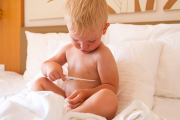 The boy sits in bed holds a thermometer in his hands