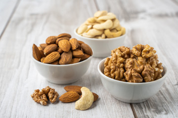 Different nuts in white bowls on wood table