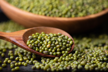 Mung bean, green moong in a wooden plate and spoon, on black metallic vintage background. Copy space. Black background. Scattered mung bean. Eco wooden spoon and plate. top view.