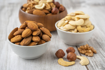 Different nuts in white and wooden bowls on wood table