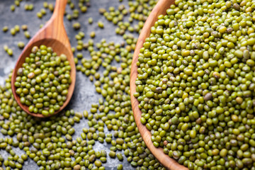 Mung bean, green moong in a wooden plate and spoon, on black metallic vintage background. Copy space. Black background. Scattered mung bean. Eco wooden spoon and plate. top view.