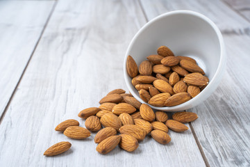 Scattered almonds seed with white bowl on wood table