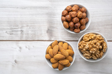 Different nuts in white bowls on wood table