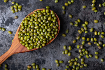 Mung bean, green moong in a wooden spoon, on black metallic vintage background. Copy space. Black background. Scattered mung bean. Eco spoon. 