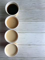 Fototapeta na wymiar Four paper cups of coffee with milk on a wooden white background close up with space for copying. Flat lay