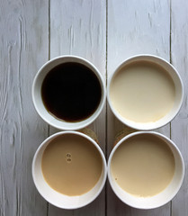 Four paper cups of coffee with milk on a wooden white background close up with space for copying. Flat lay