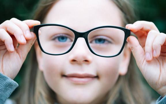 Closeup portrait of little girl  with myopia correction glasses. Girl is holding her eyeglasses right in front of camera with two hands - focus on glasses - shallow depth of field
