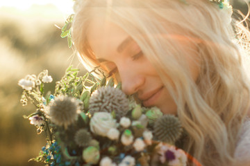 Beautiful young woman portrait in a white dress in boho style with a floral wreath in the summer in the field. Selective soft focus. © Roman