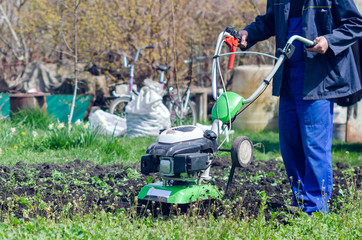 A man plows the land with a cultivator in a spring garden