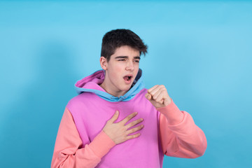 portrait of young teenage man isolated on blue background coughing