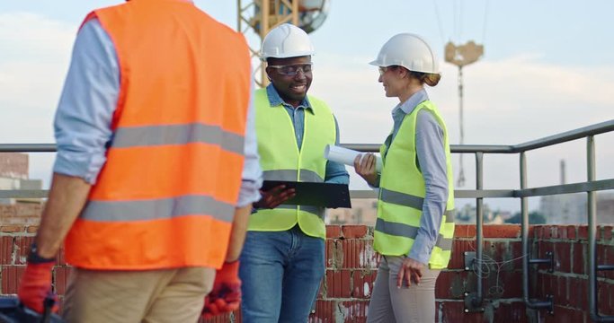 Young African American man constructor with tablet computer in hands talking with Caucasian woman architect at the building site outside on a working day.
