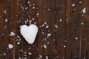 a snowball in the shape of a heart lying on the dark wooden boards covered with flakes of snow