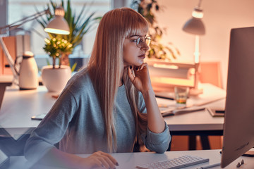 In the nice office blond woman in glasses is focused on computer while doing her job.