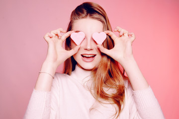 The girl closes her eyes with hearts, the girl is in love, Valentine's Day. The blonde on a pink background, surprised, excited, smiling, having fun. March 8, Women's Day.