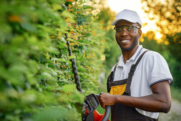 Happy african man cutting bushes with petrol hedge trimmer