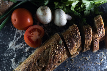 Closeup on a black background french baguette with sesame seeds, mushrooms and tomatoes