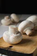 still life, champignon mushrooms on a cutting wooden board with black background