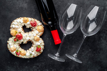 a cake in the shape of 8 is decorated with flowers, cream cheese, marshmallows, Bizet with a bottle of wine and glasses on a stone background. holiday concept dinner for two on March 8.