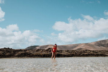 Fototapeta na wymiar woman walking on beach and volcanic rocks