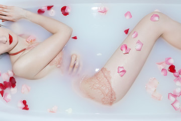 Obraz na płótnie Canvas Young sexy girl taking a milk bath with rose petals