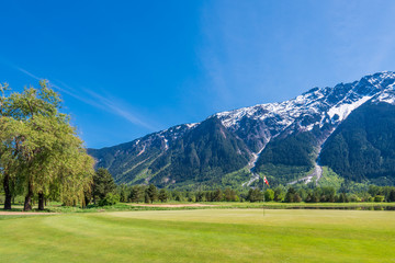 Fototapeta na wymiar Golf course with flag, gorgeous pond and fantastic snow mountain view.