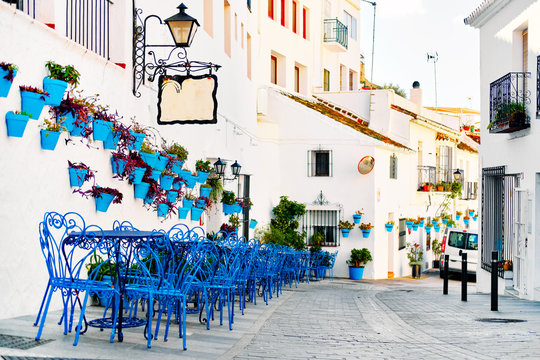 Mijas Pueblo Blanco, charming small village, picturesque empty street in old town with bright blue tables chairs of local cafe, flower pots hanging on white washed houses walls, Costa del Sol, Spain
