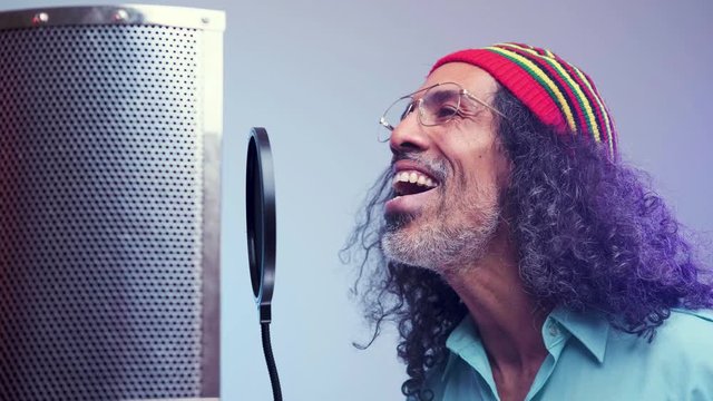 Attractive middle aged man with long hair is singing next to microphone.