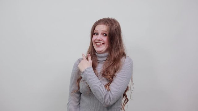 a young beautiful red-haired woman in a gray sweater smiles and points her index finger in the direction, happy and satisfied