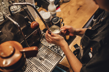 Barista steaming milk for coffee in coffee shop. Coffee maker