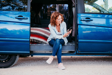 happy woman sitting in a blue van and having fun. travel concept. woman using mobile phone © Eva