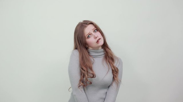 A young, beautiful, red-haired woman in a gray sweater looks guiltily ahead, her eyes narrowed and her lip bitten