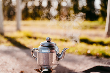 close up view of a teapot with hot tea in stove. camping concept