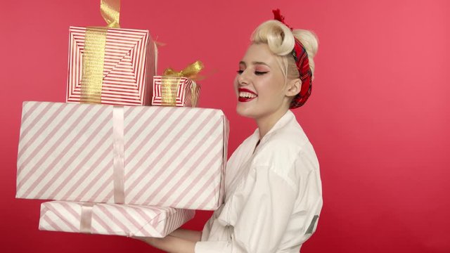 Laughing pin up girl holding present boxes on pink background