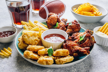 Table fof tasty snacks for beer prepared for watching sports on TV. Chicken. Chicken wings, chicken nuggets, french fries, chips, various sauces and lemonade. Light gray background. Selective focus