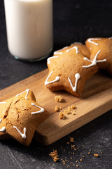 Handmade custard gingerbread in the shape of a star on a black background. Homemade baking. A bottle of milk in the background. Wooden plank. Baking crumbs.
