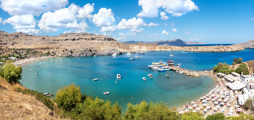 Small beach in Lindos bay with holidaymakers and pier with tourist boats  (Rhodes, Greece)