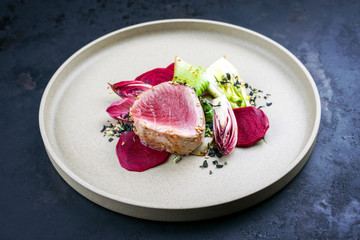 Japanese gourmet fried tuna fish steak tataki with pak choi, witloof and red beet offered as closeup on a modern design plate