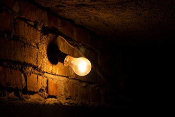 Light bulb on brick wall. Light bulb glowing in dark. Incandescent light bulb on a dark wall...