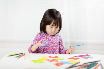 toddler girl practice writing letters on white paper against white background