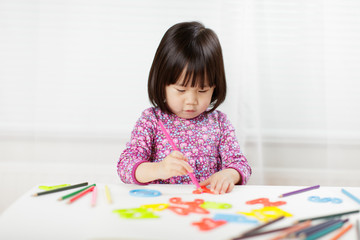 toddler girl practice writing letters on white paper against white background